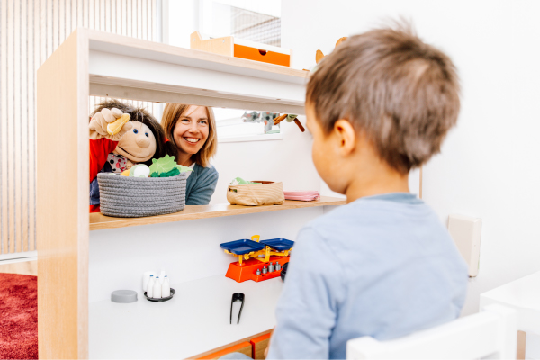 Während einer Logopädie-Sitzung in Kiel interagiert eine Frau mithilfe einer Handpuppe mit einem kleinen Jungen über eine Spieltheke hinweg.
